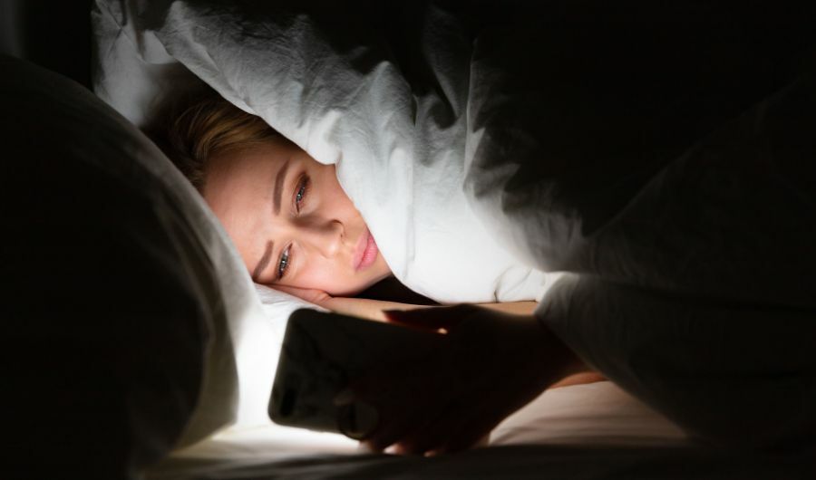Sad woman in the bed stares at her mobile phone