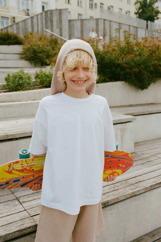 мальчик в бежевых шортах и белой длинной футболке с худи на голове