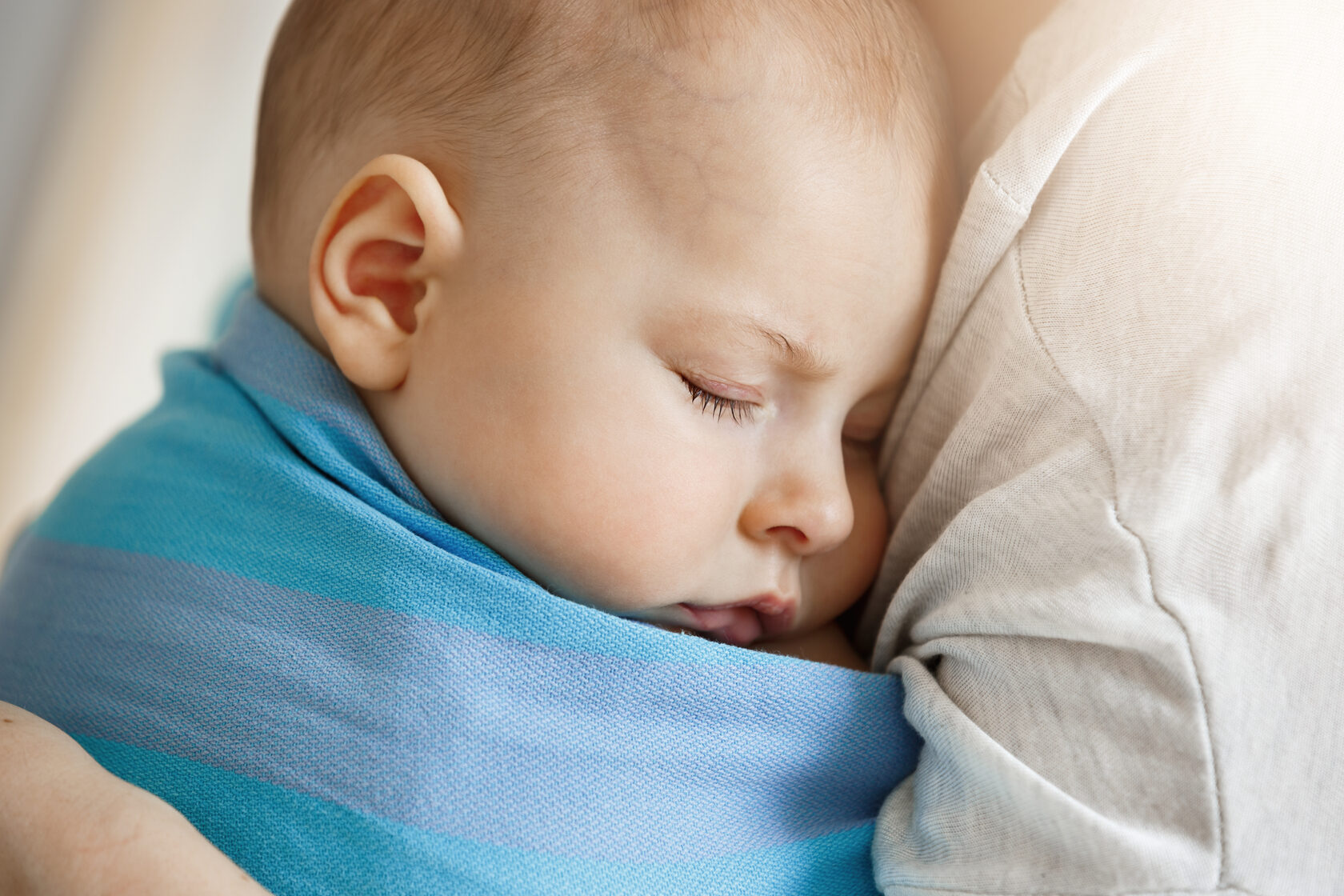 Newborn baby peacefully sleeping in a blue wrap on parent’s chest, showing secure attachment and comfort