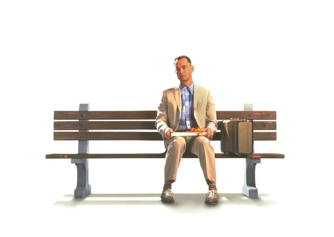 Кадр из фильма Форрест Гамп: мужчина в светлом костюме сидит на скамейке с коробкой шоколадных конфет — иллюстрация к фразе «Life is like a box of chocolates»