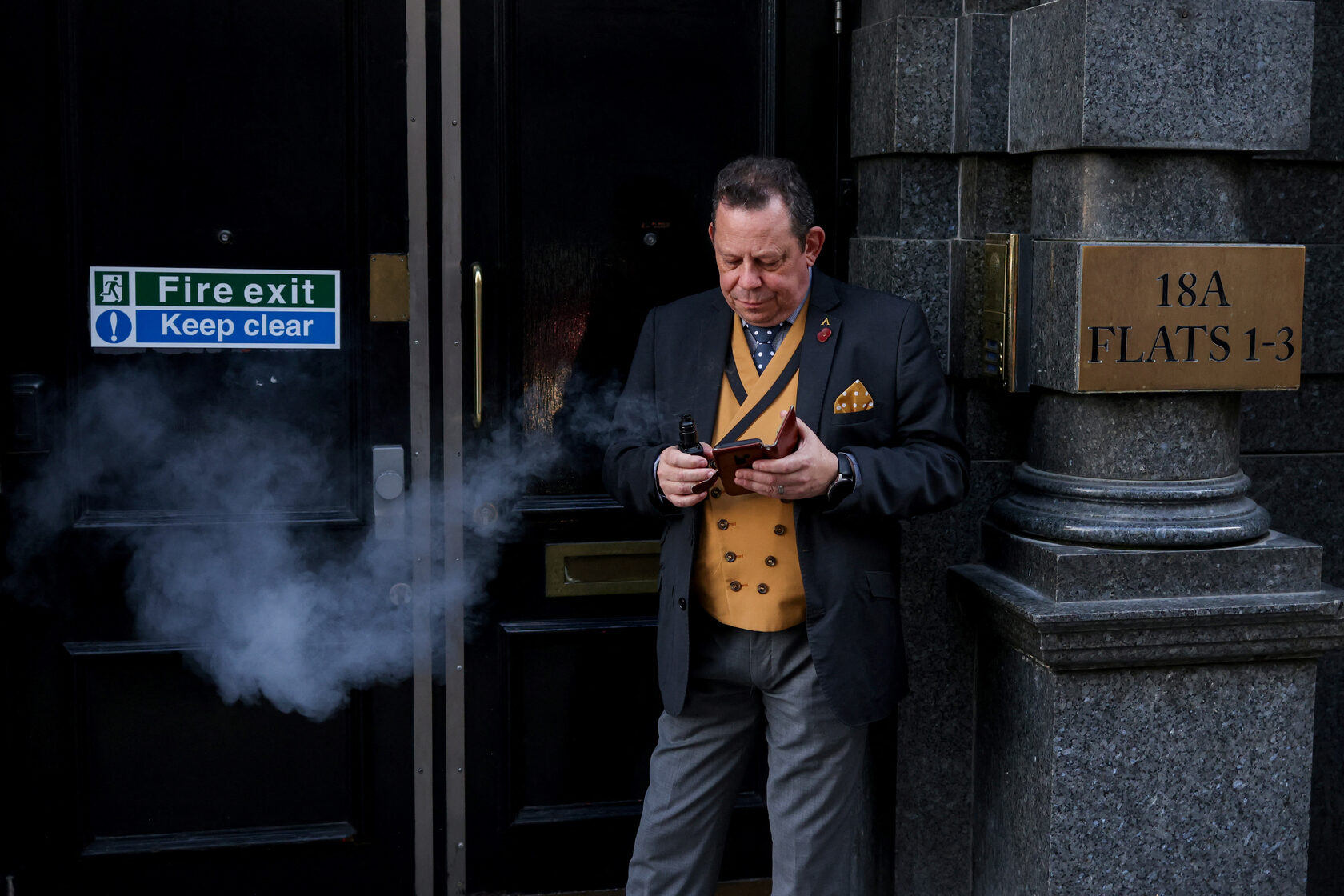 A man smokes an e-cigarette in a fire escape doorway