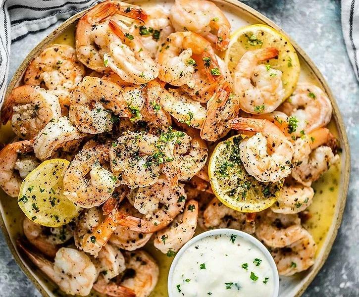 запеченные креветки с лимоном, специями и соусом на блюде