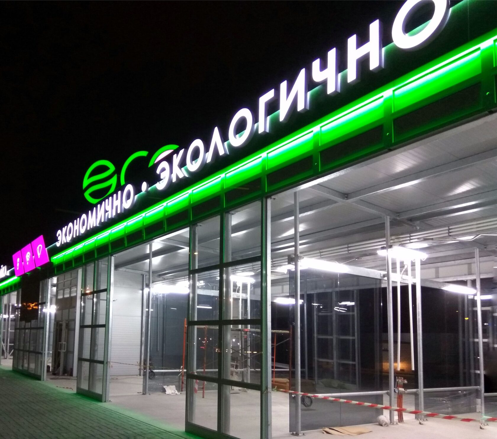 Светящаяся вывеска «eco Экологично» с зелёной подсветкой на фасаде ночью
