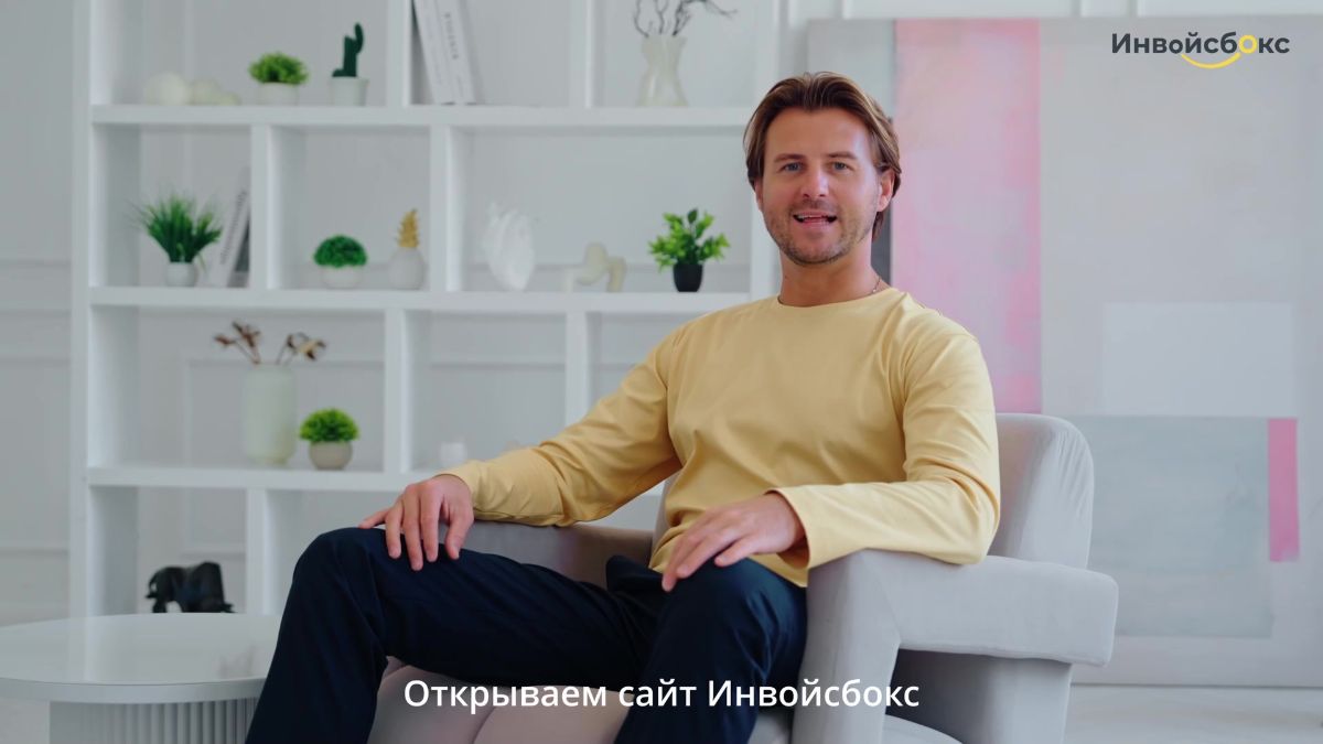 Кадр из ролика «Инвойсбокса»: ведущий в кресле в светлой комнате, субтитр «Открываем сайт Инвойсбокс»
