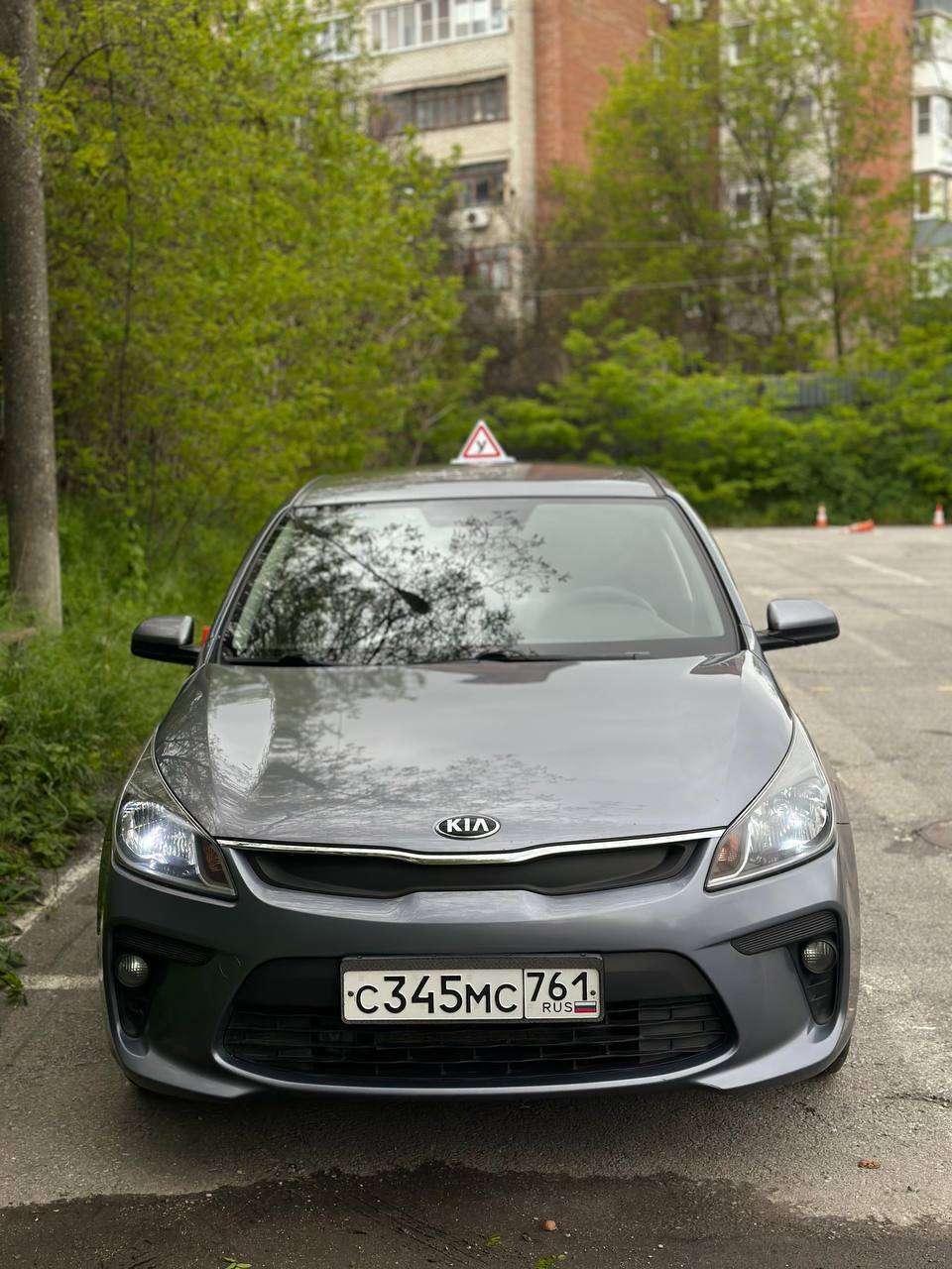 Серый учебный Kia Rio с включёнными фарами на учебной площадке