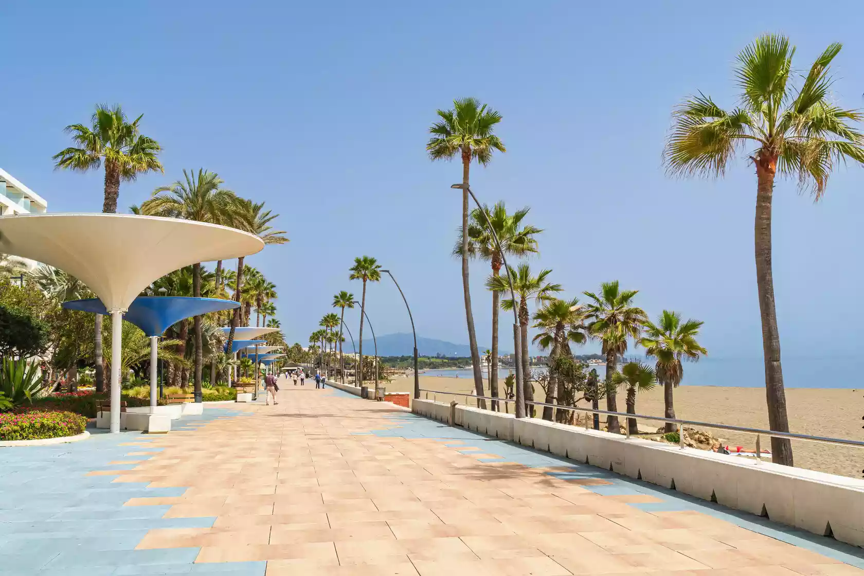An idyllic stretch of coastline with golden sands, sparkling blue waters, and a boardwalk lined with sun loungers and umbrellas, capturing the essence of a Spanish beach paradise.