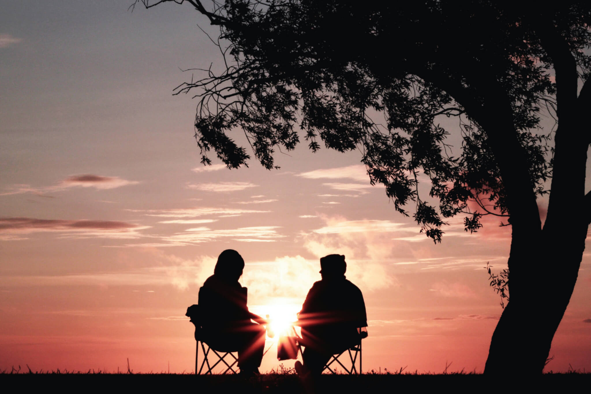 Zwei Personen sitzen entspannt in der Natur in Campingstühlen und betrachten den Sonnenuntergang