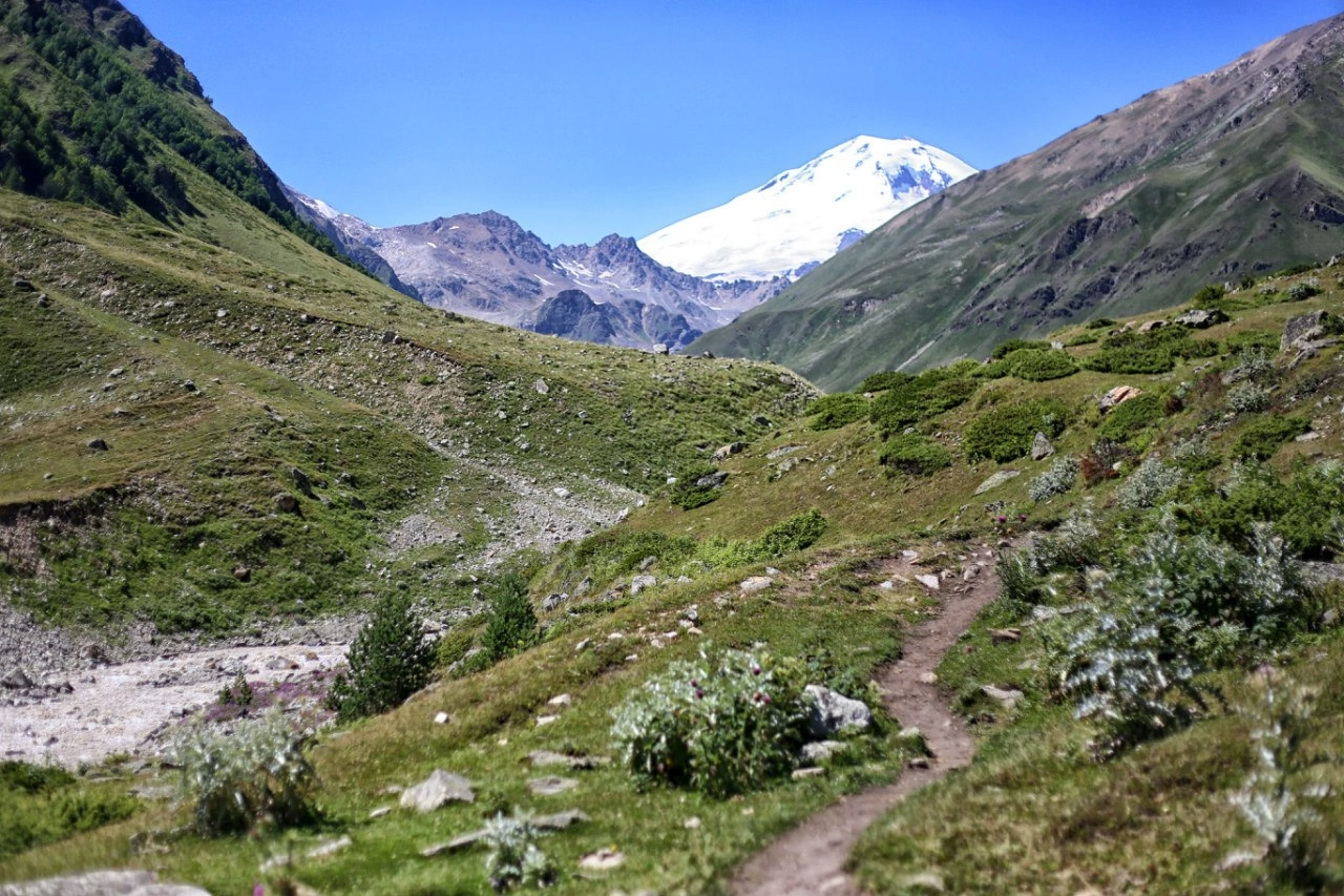 Hiking path in a green valley with snow-capped Elbrus in the distance