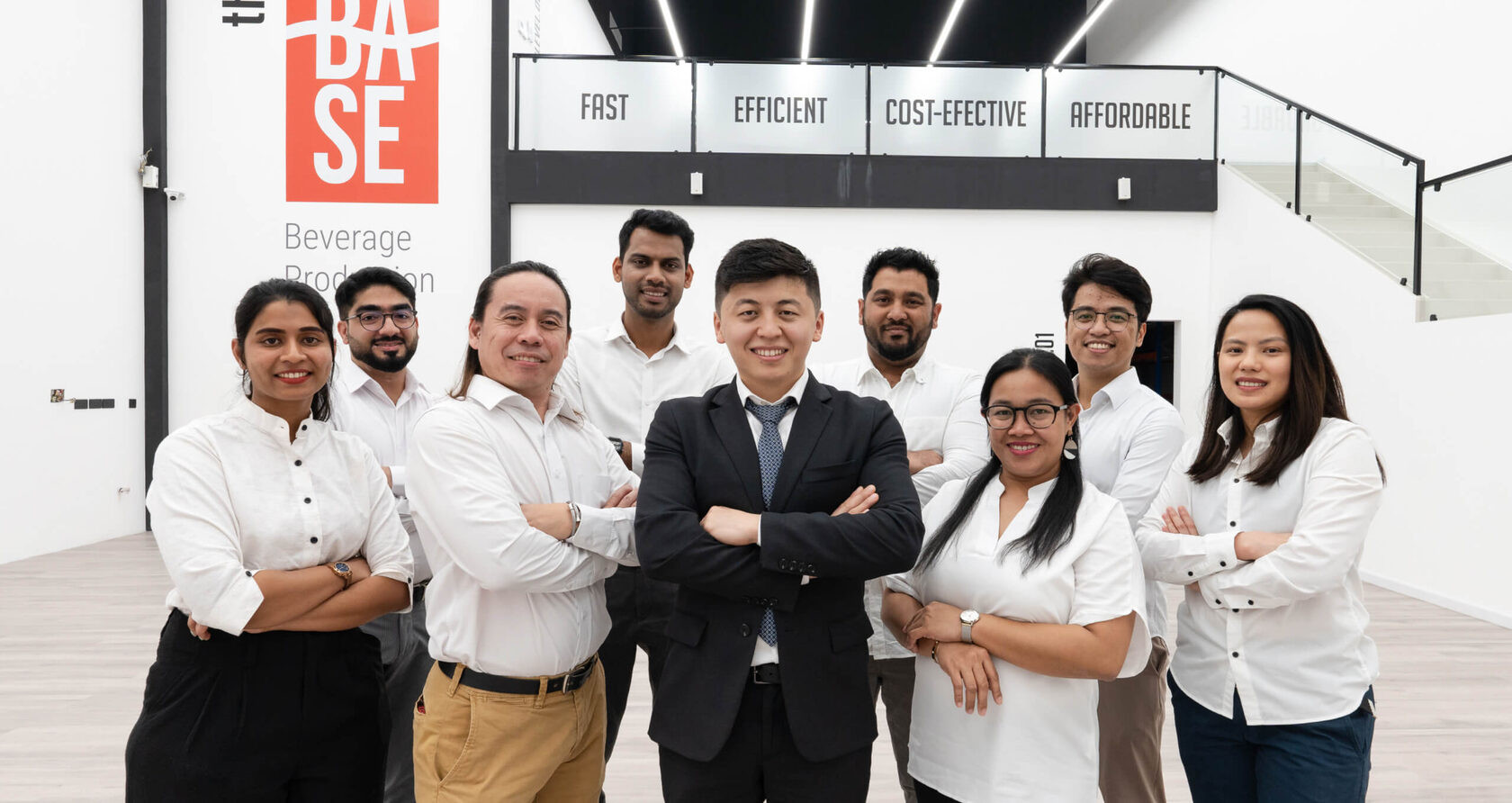 The Base Beverage team at the Dubai production facility in front of the Fast, Efficient, Cost-effective, Affordable wall