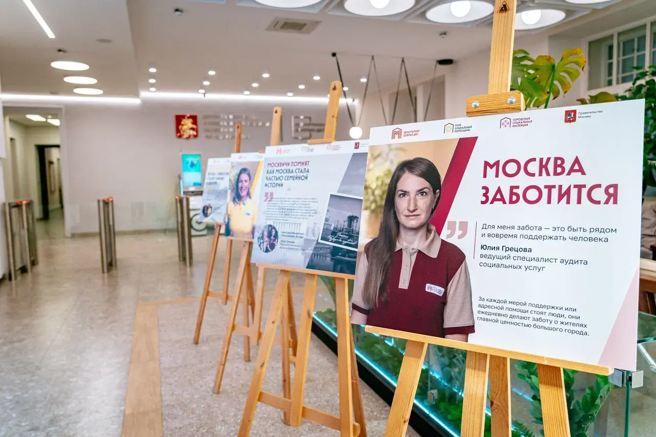 Выставочные мольберты в холле Департамента труда и социальной защиты. Крупным планом представлен плакат фотовыставки «Москва заботится. Москвичи помнят» с Юлией Грецовой, ведущим специалистом аудита социальных услуг.