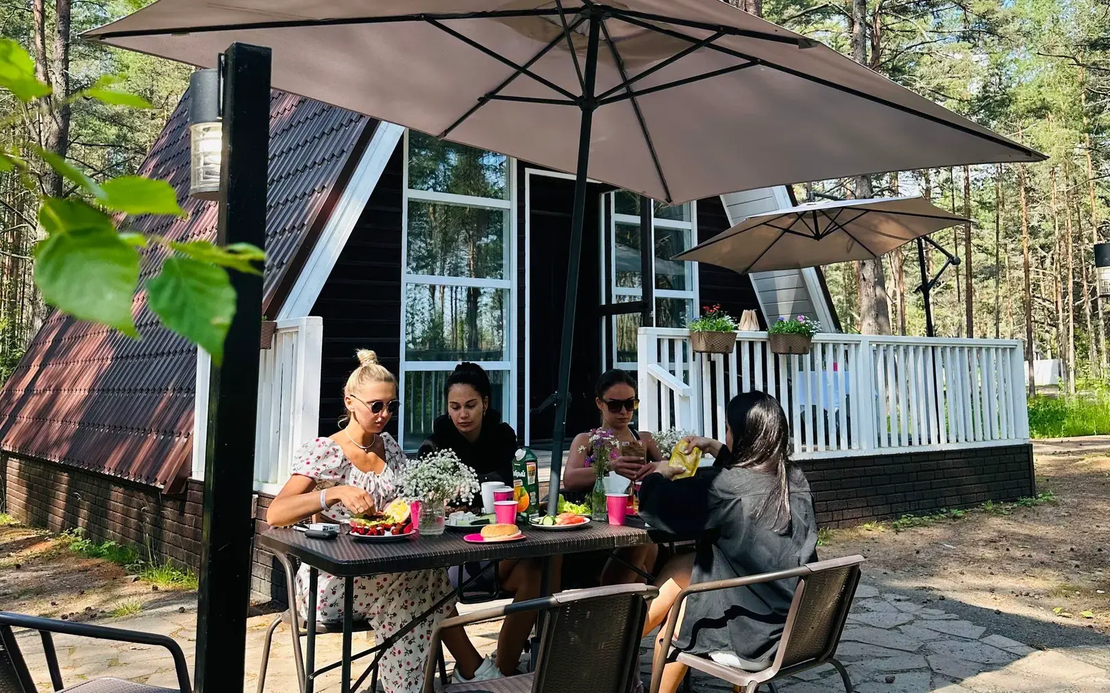 Компания обедает на террасе у коттеджа A-Frame Family под зонтом