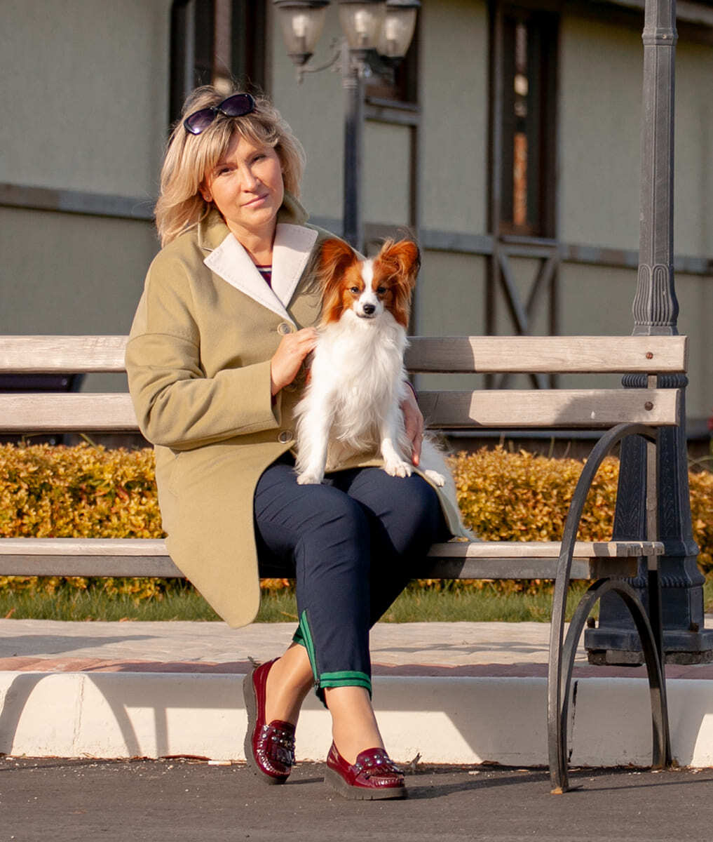 женщина с папийоном на руках сидит на лавочке