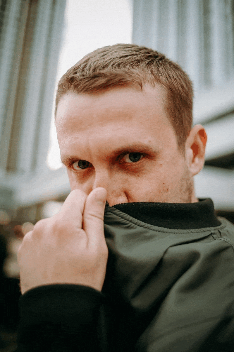 Ваня прикрывает половину лица воротом куртки и смотрит в камеру