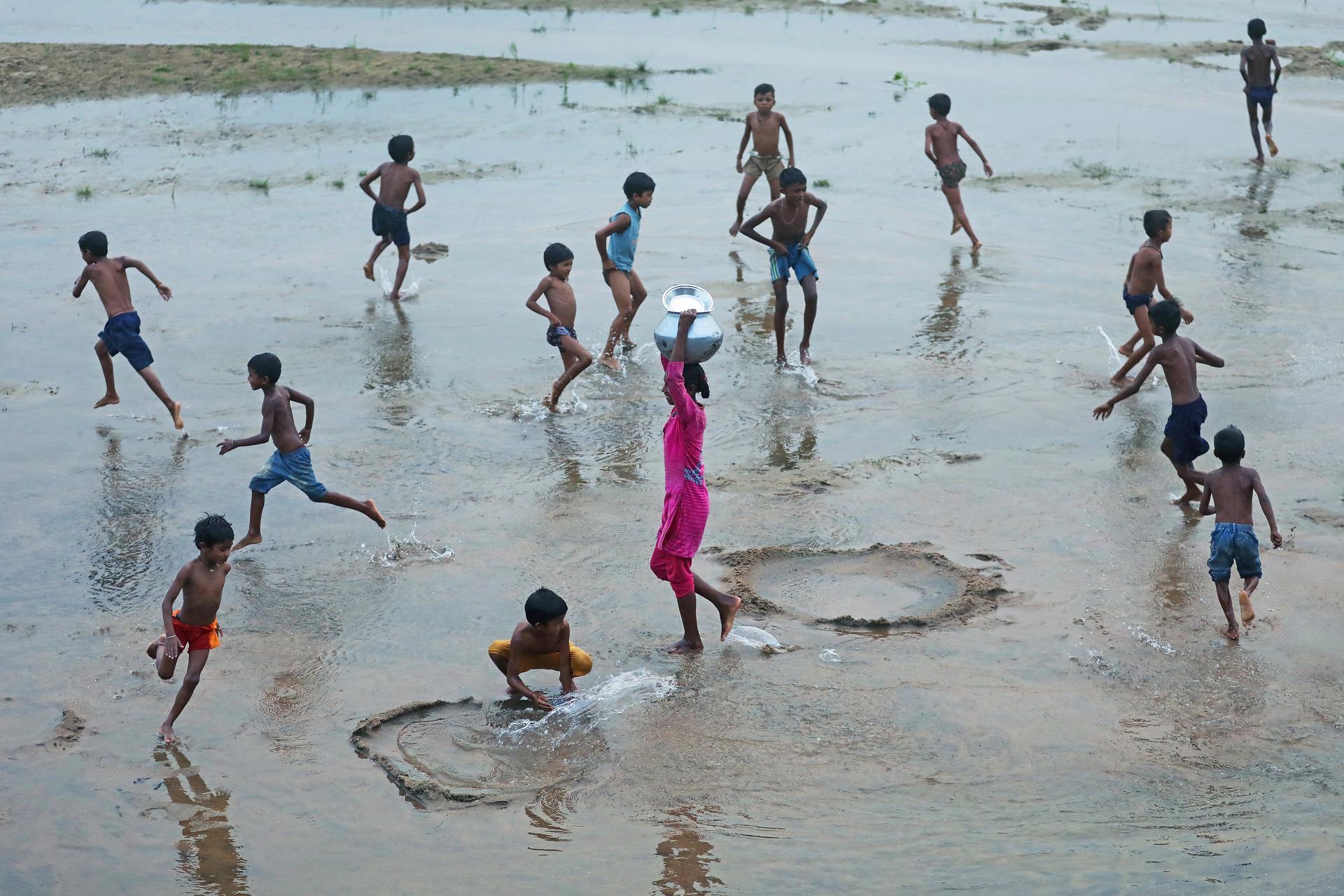 India | Barun Rajgaria. A young woman walks to collect water as children play around her in a rural community.