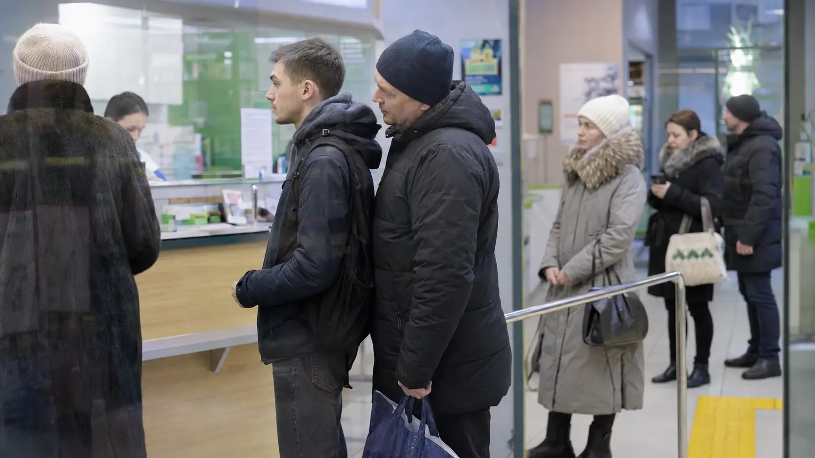 Посетители стоят в очереди у стойки, сохраняя дистанцию и личное пространство.