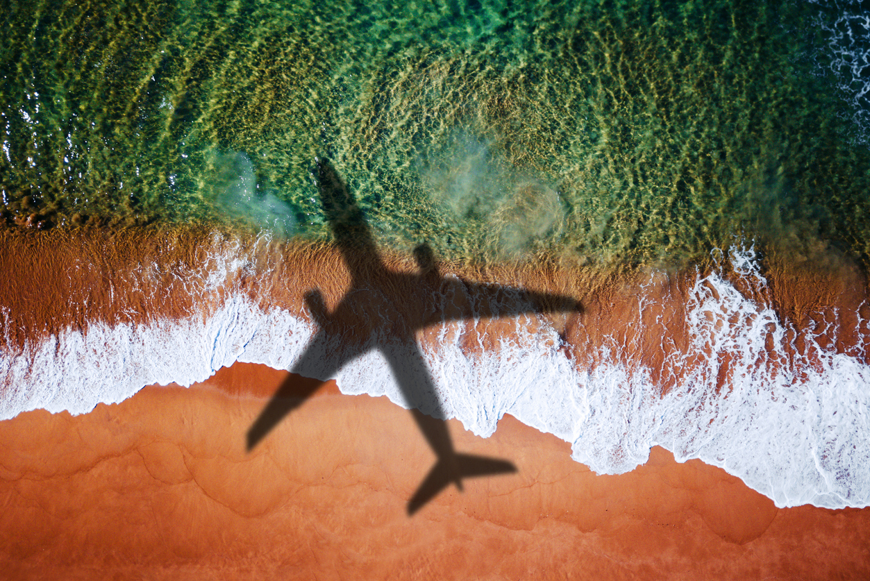 Airplane shadow flying over the crashing waves of a beach.