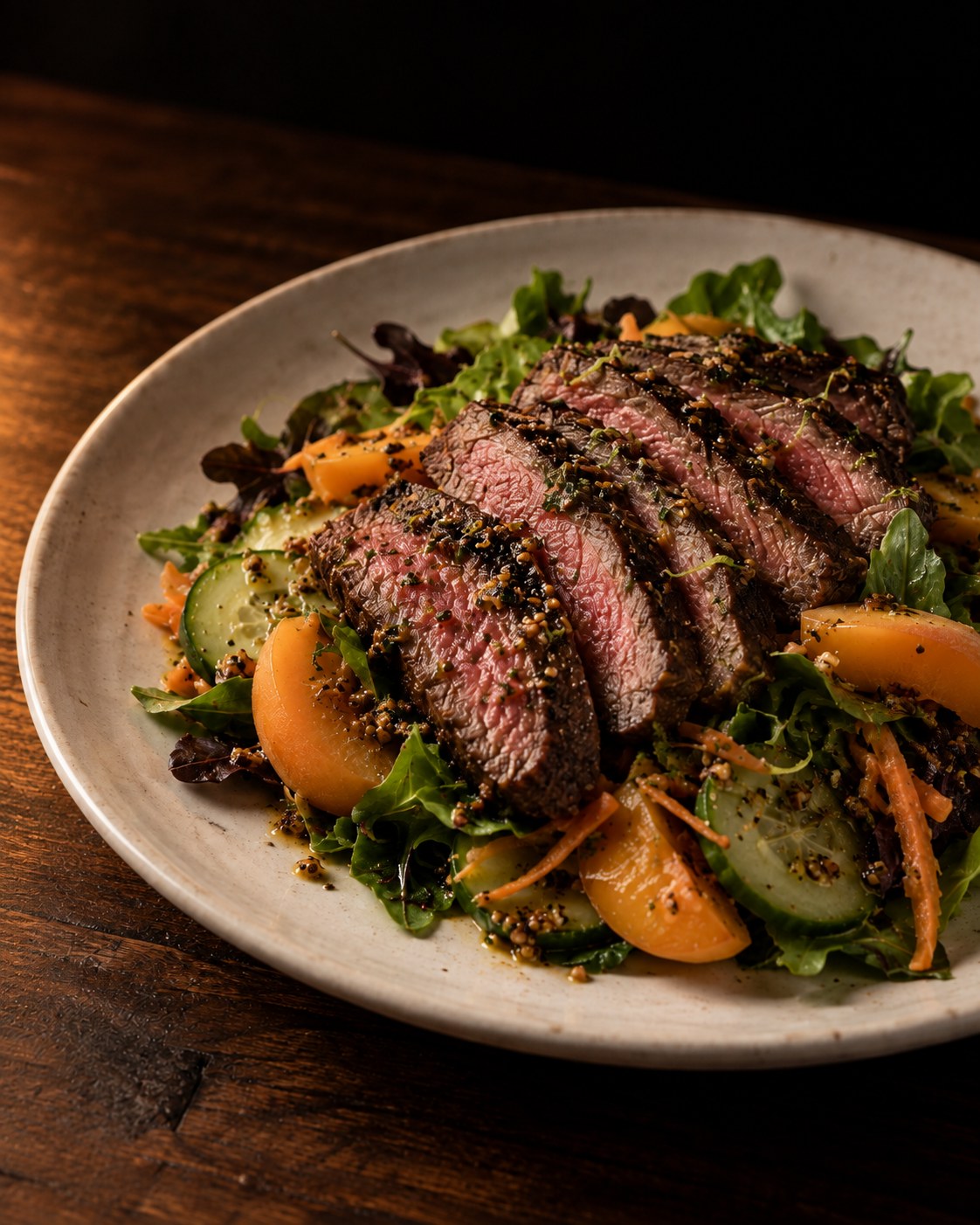 Slices of seared steak over a salad of apricots, cucumber, grated carrot and greens with a grainy mustard dressing on a white plate, by Miami private chef Marina Staver