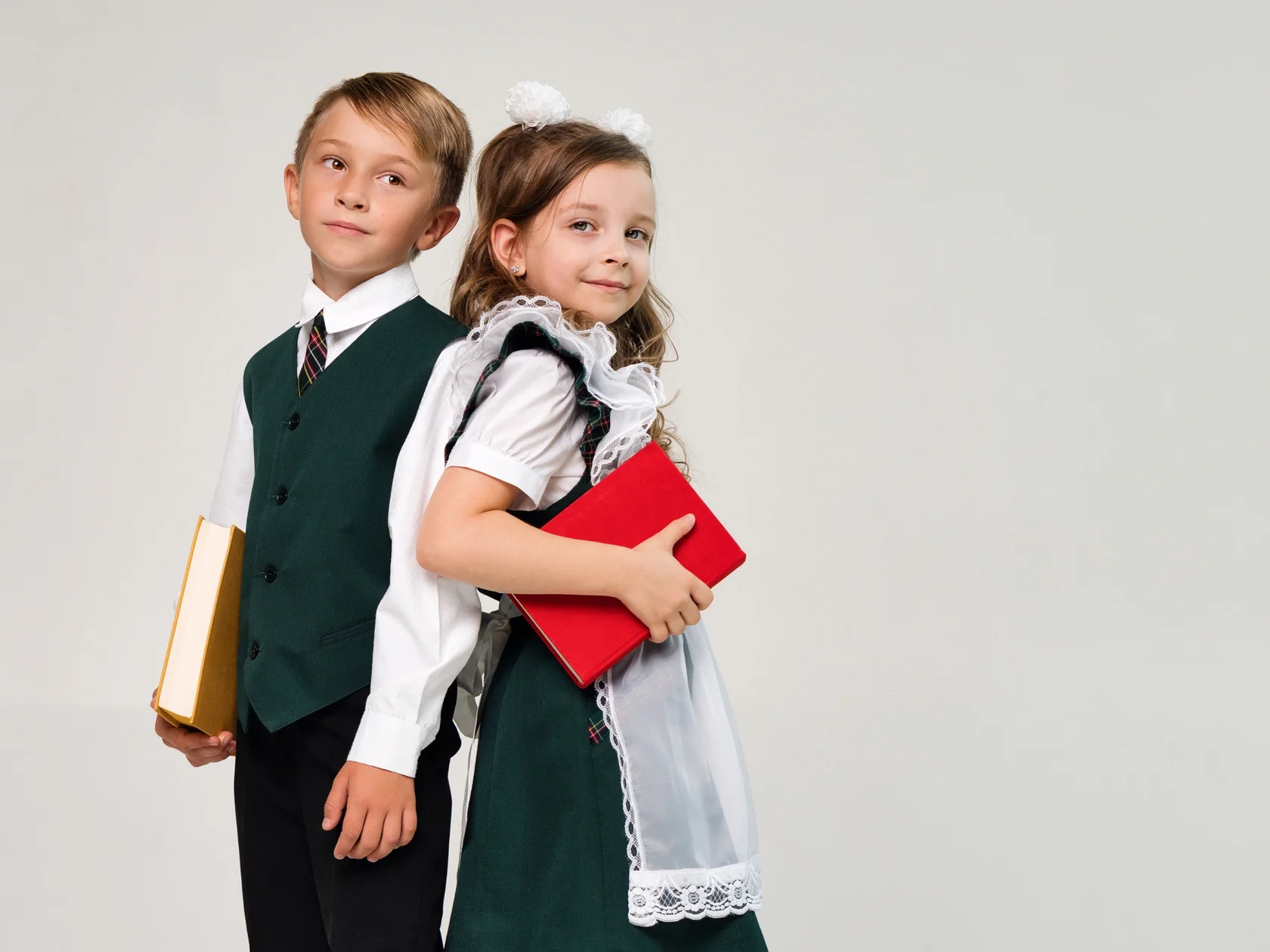 Два первоклассника в школьной форме с книгами — здоровье зубов детей, профилактика повреждения эмали, влияние кислотных напитков и фруктов.