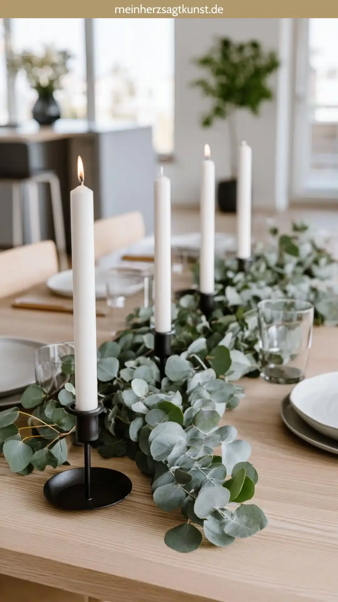 Современное оформление стола: гирлянда из эвкалипта и простые белые свечи на светлом деревянном столе.