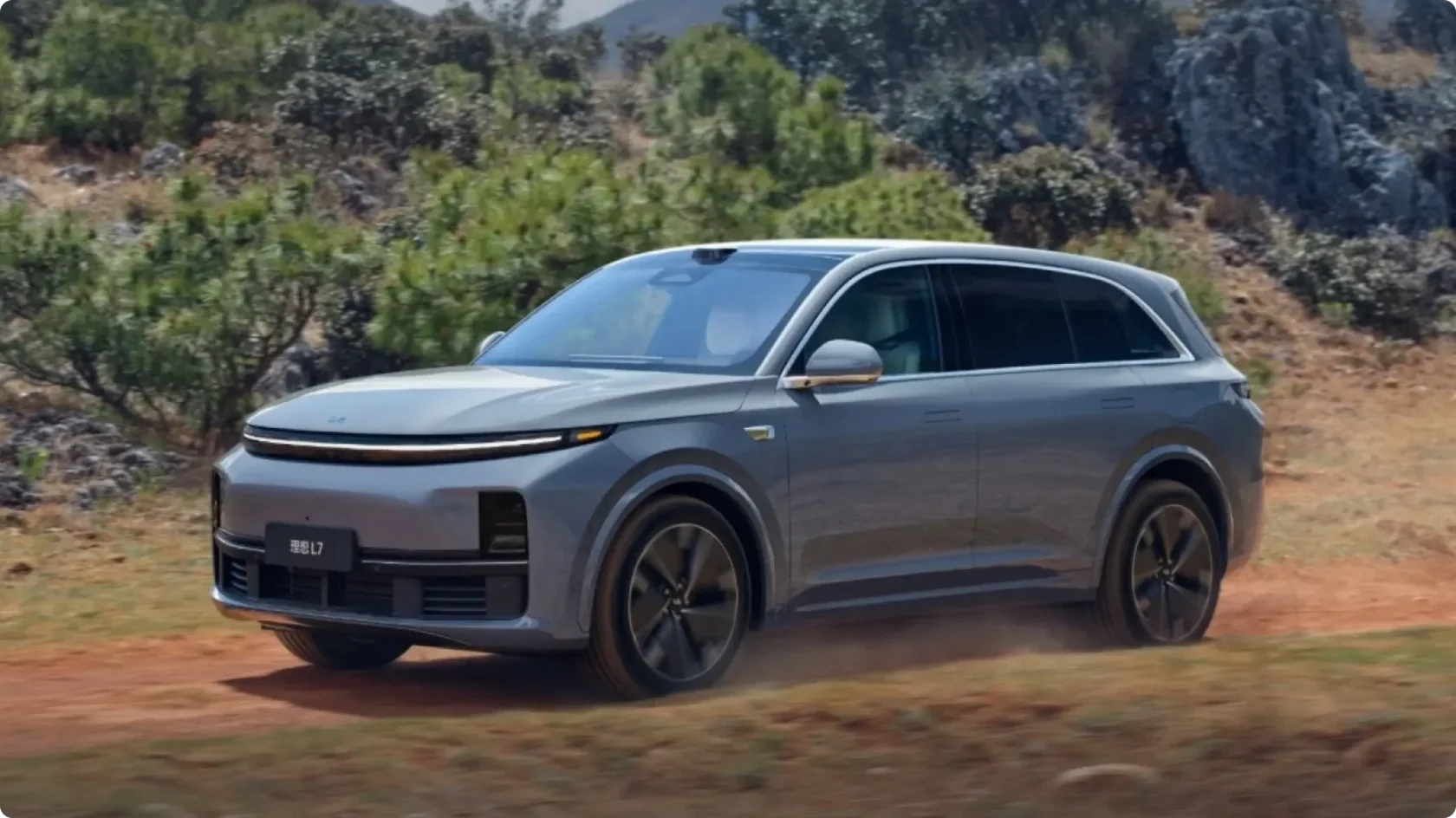 Обновленный гибридный кроссовер Li Auto L7 в серо-голубом цвете в движении по грунтовой дороге, вид спереди сбоку: светодиодная полоса, лидар на крыше и пневмоподвеска.