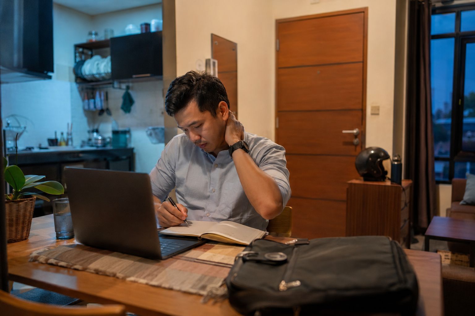 Pekerja Indonesia duduk di depan laptop setelah pulang kerja dengan wajah terlihat lelah
