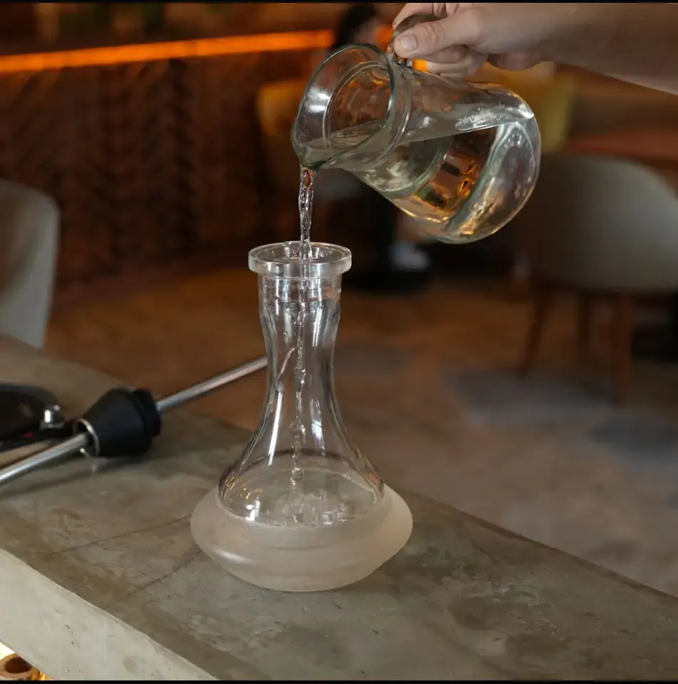 Pouring water into a glass hookah base