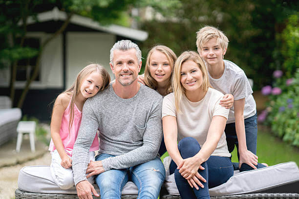 A family of five posing for the camera on a bench outside their home