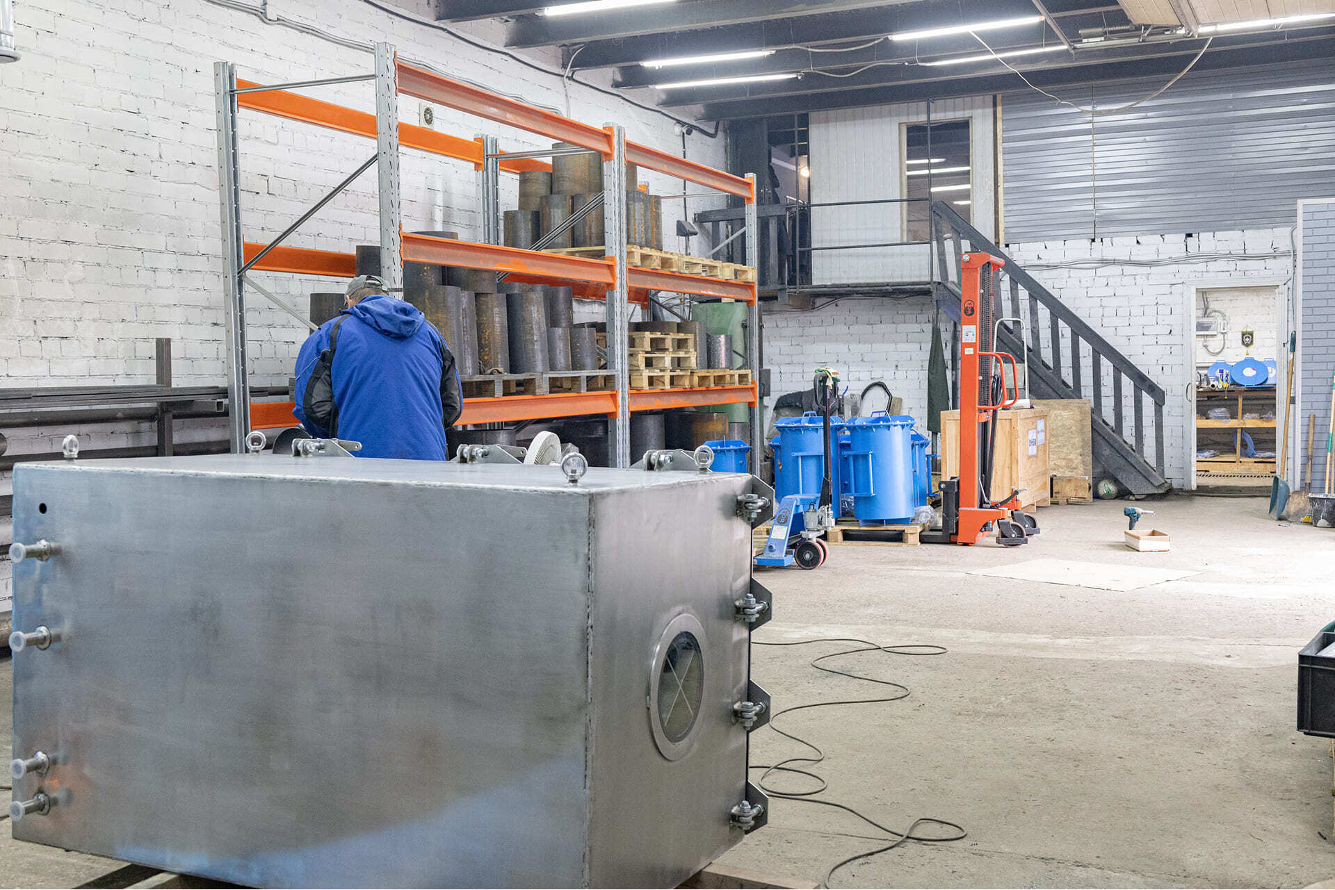 Рабочий в цехе готовит к сборке крупную вакуумную камеру из нержавеющей стали.