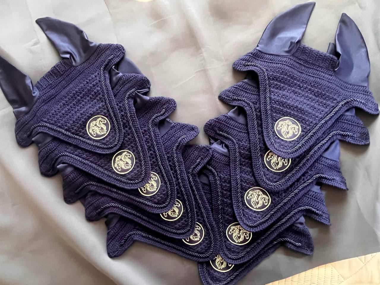 Navy blue hand-knitted ear bonnets with metal horse badges, made in bulk