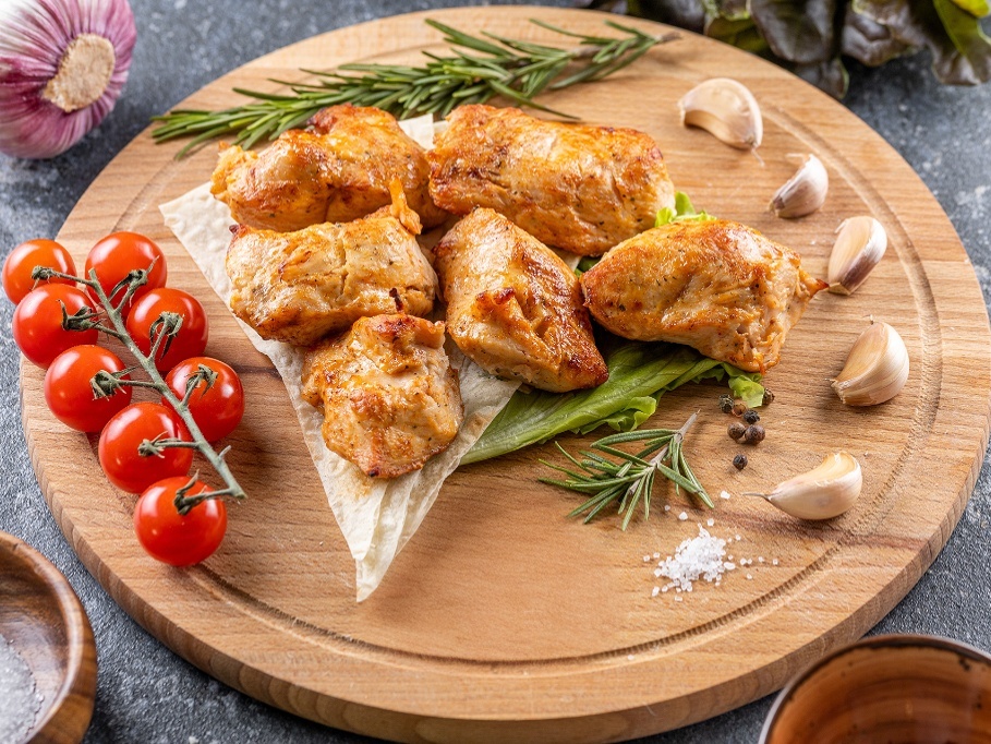 Куски индейки на деревянной доске с томатами и чесноком
