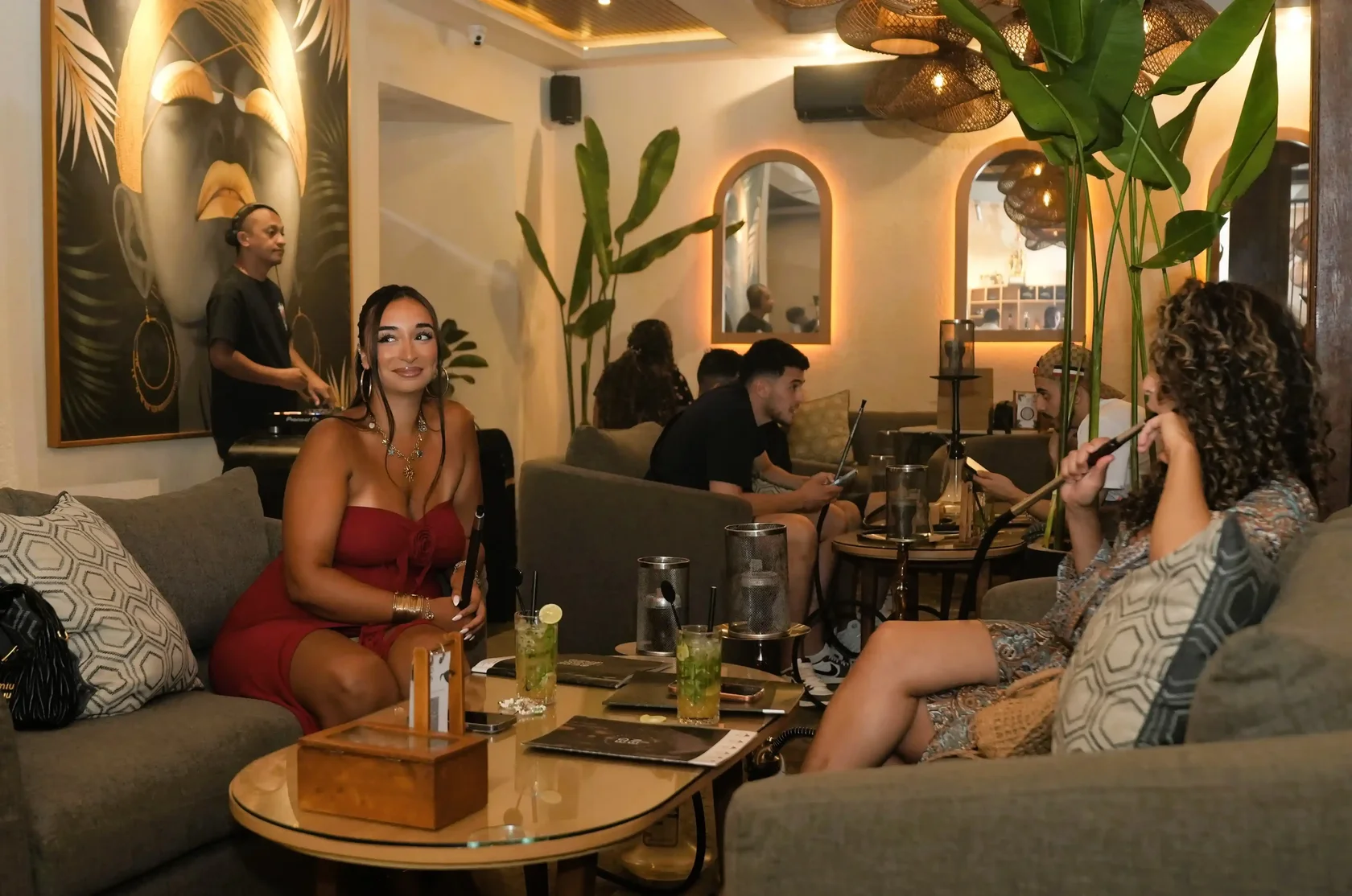 A relaxed group of friends sits on comfortable sofas, enjoying hookahs and vibrant cocktails under soft lighting in a modern Bali lounge, showing what makes a great Wednesday night out on the island.