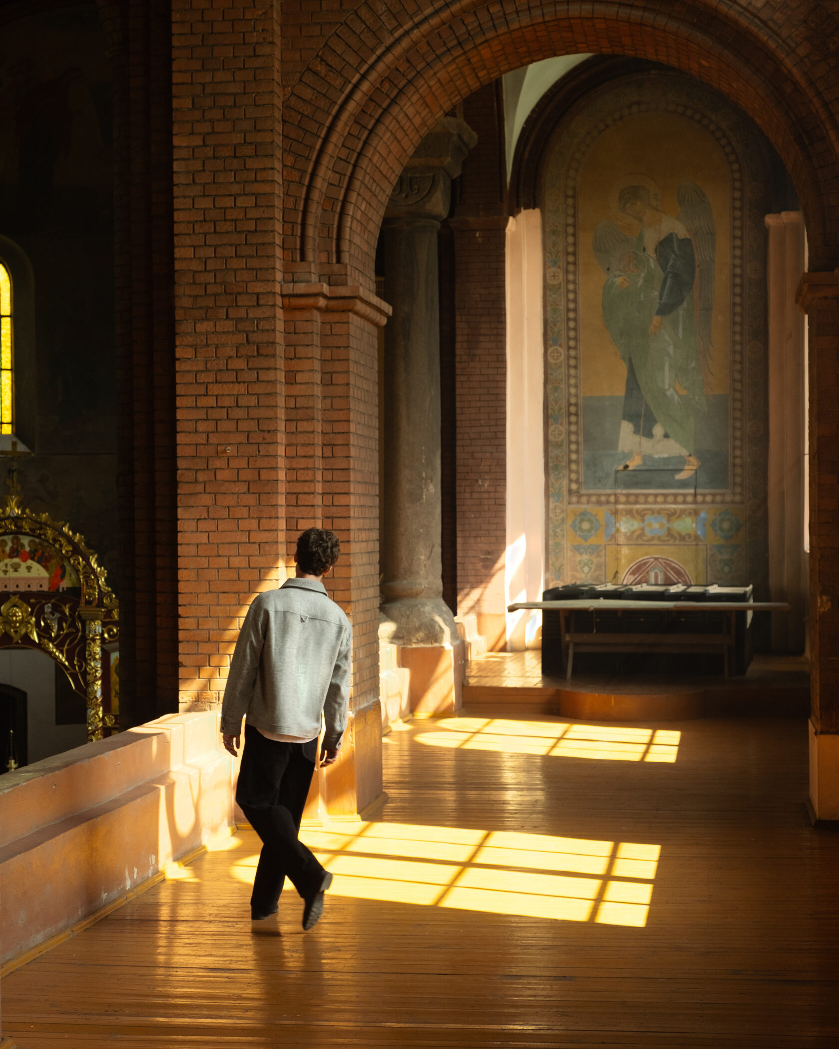 Мужчина в серой куртке идёт по церкви с кирпичными арками