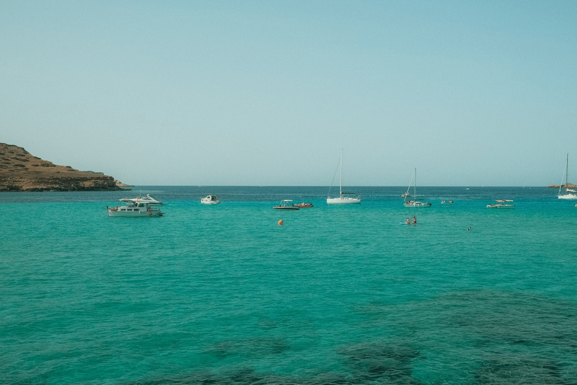 sunny beach with people swimming in the clear blue sea