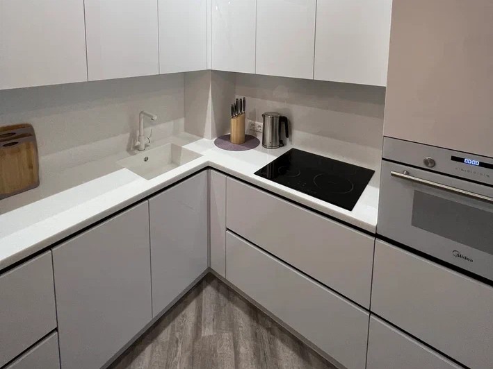 Кухня с комплексной меблировкой Сургут — угловая планировка, белые фасады, встроенная техника, столешница из камня