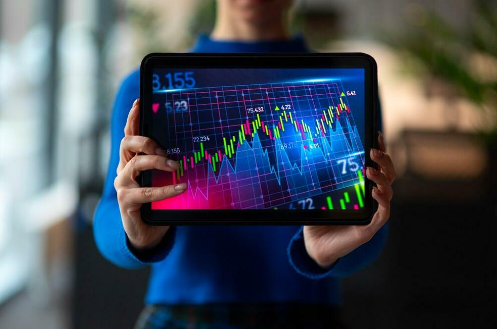 A person holding a digital tablet with trading chart patterns