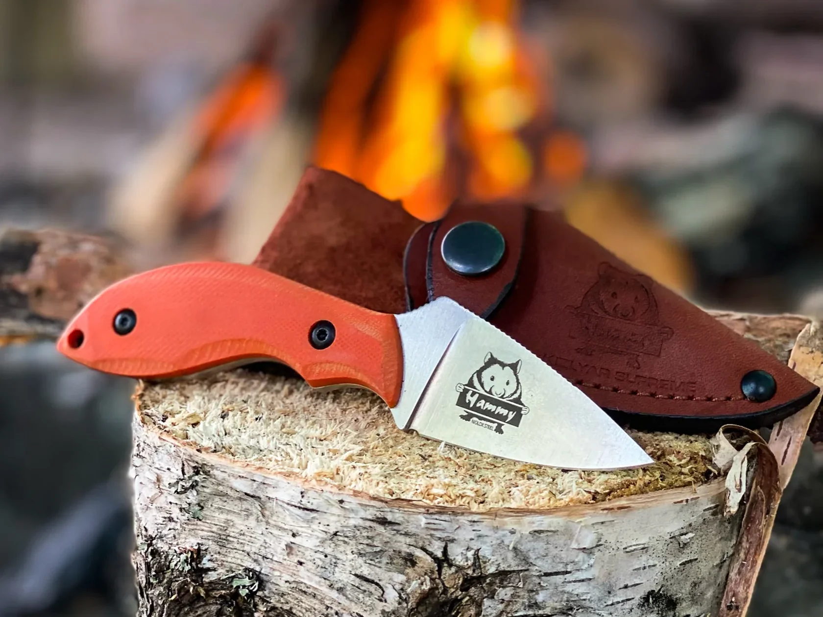 Hammy compact fixed blade with orange G10 beside a campfire
