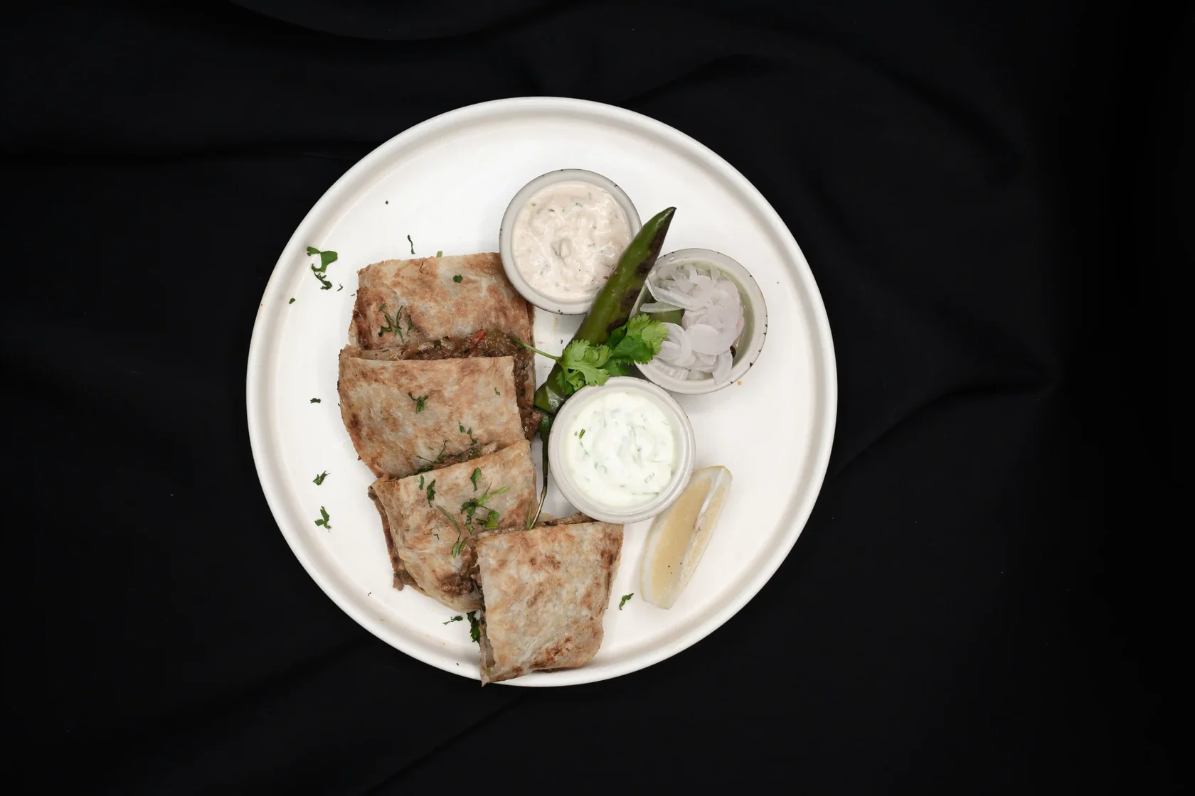 Arabic Mutabbaq Pocket filled with minced beef, leek, tomato, and egg. Served with green chili chutney, yogurt chutney, lemon, pickled onion, and grilled green chili