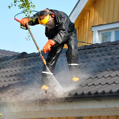 Альпинист на крыше дома почищает водосток водой под давлением