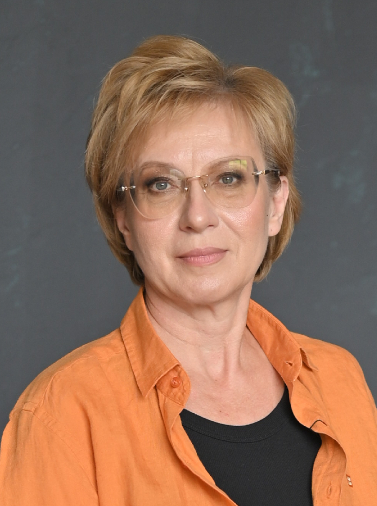 Спикер Ольга Антошина в оранжевой блузке, фотография анфас, нейтральный серый фон