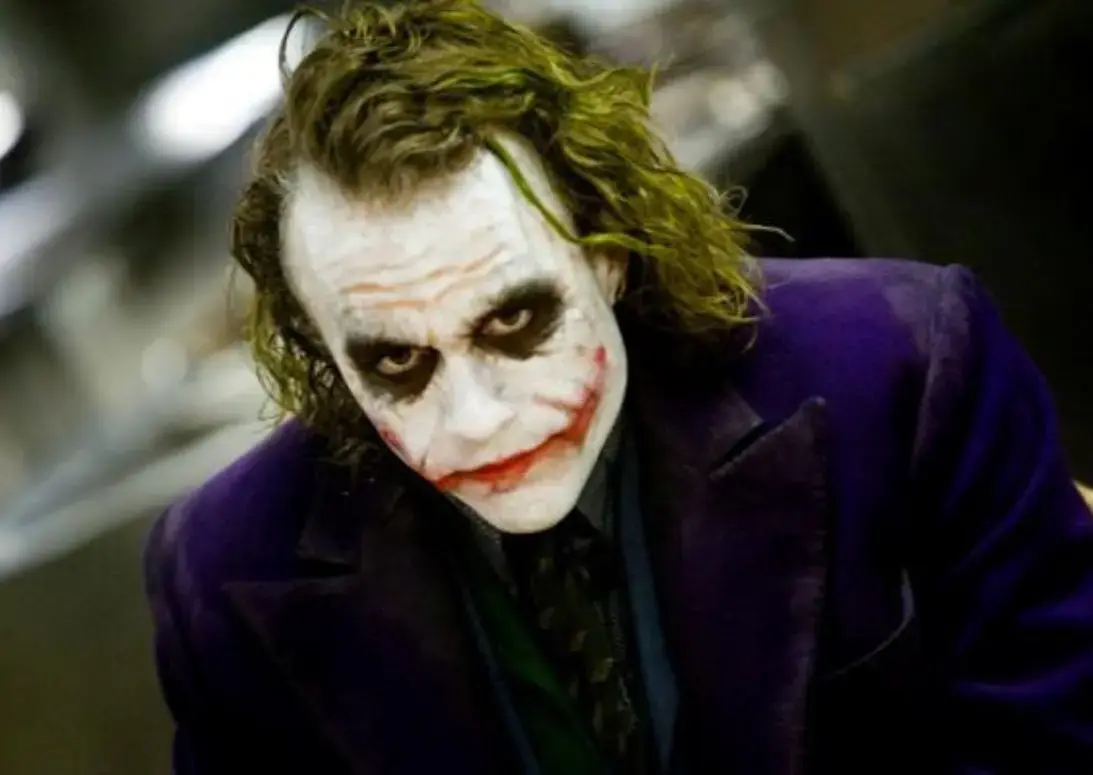 Мужчина с размазанным гримом и устрашающей улыбкой в тёмном костюме смотрит прямо в камеру — кадр из фильма с фразой «Why so serious?»