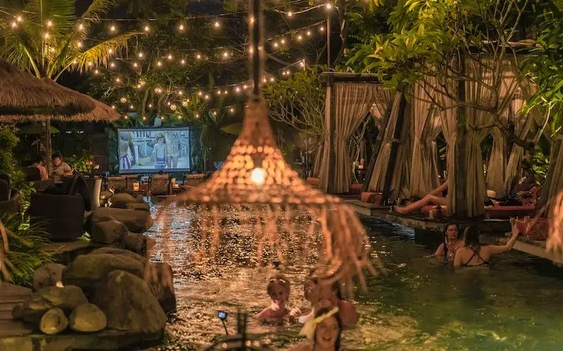 Guests relaxing in the pool at night while watching a large outdoor screen at Folk Ubud, offering a beautifully unique setting for where to watch a movie in Bali.