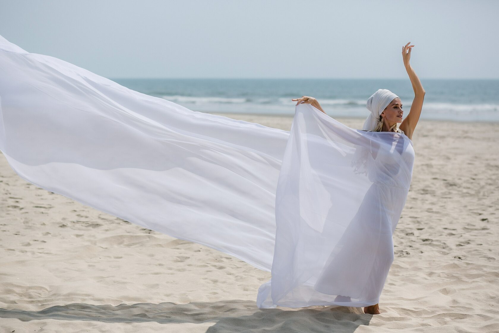 Maya Mandala dancing in a white headscarf with a long flowing veil on the seashore, full length