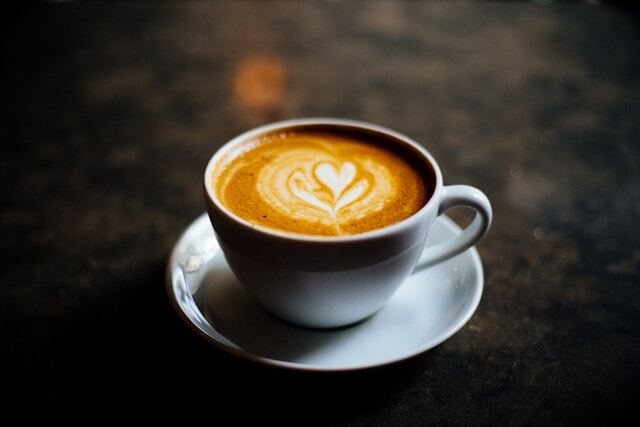 A cup of coffee on a dark wood table. The cup and saucer are white and there&amp;amp;amp;amp;#39;s no biscuit