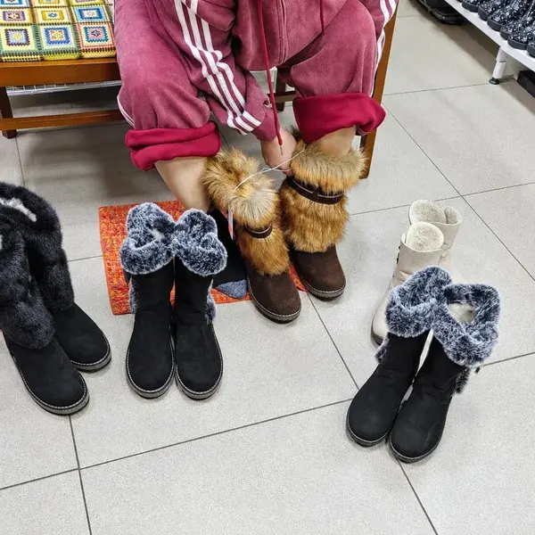 Покупатель примеряет коричневые унты, рядом стоят другие пары обуви