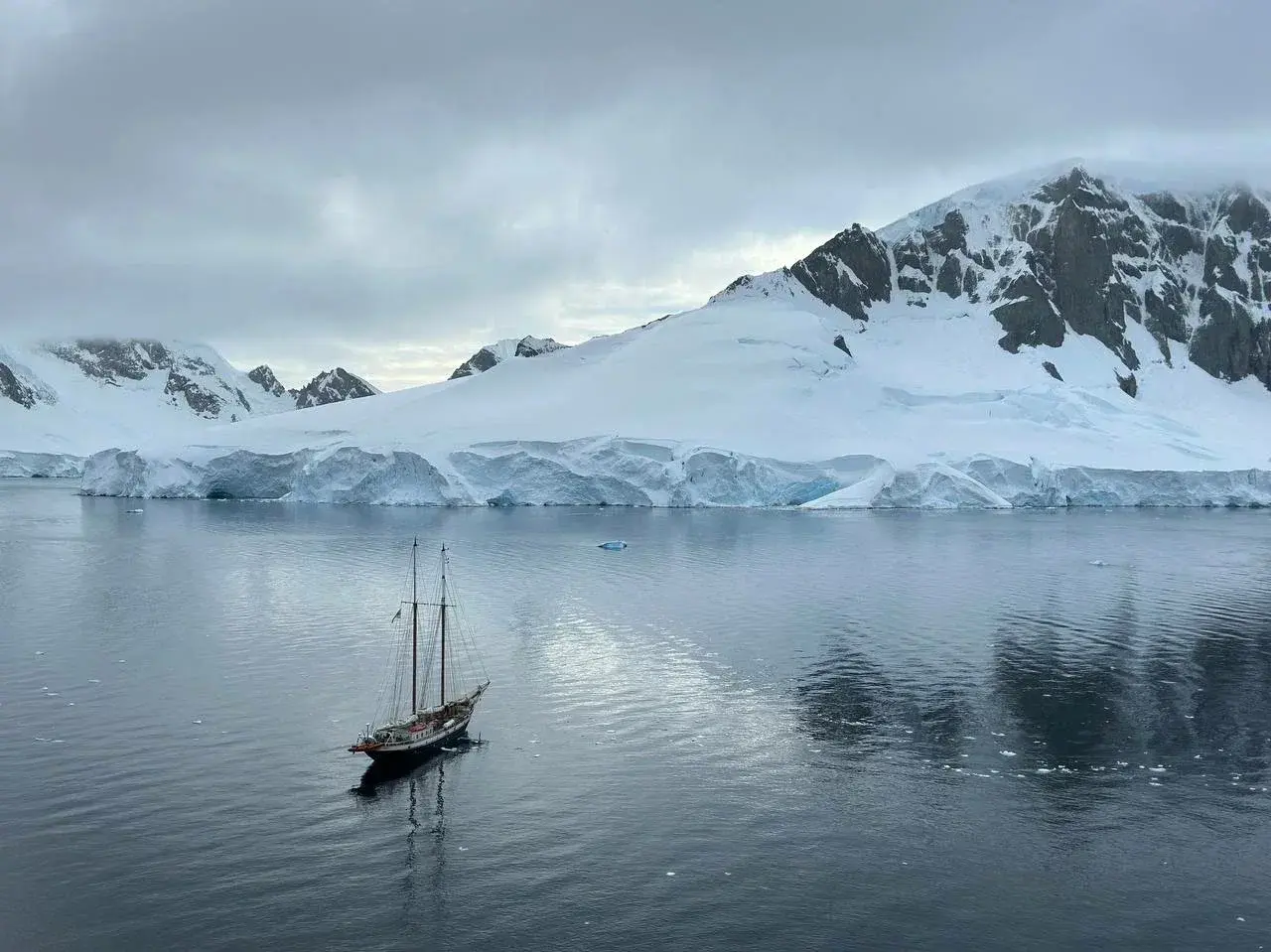 Traditional expedition schooner sailing through Antarctic waters surrounded by glaciers and snow-covered mountains