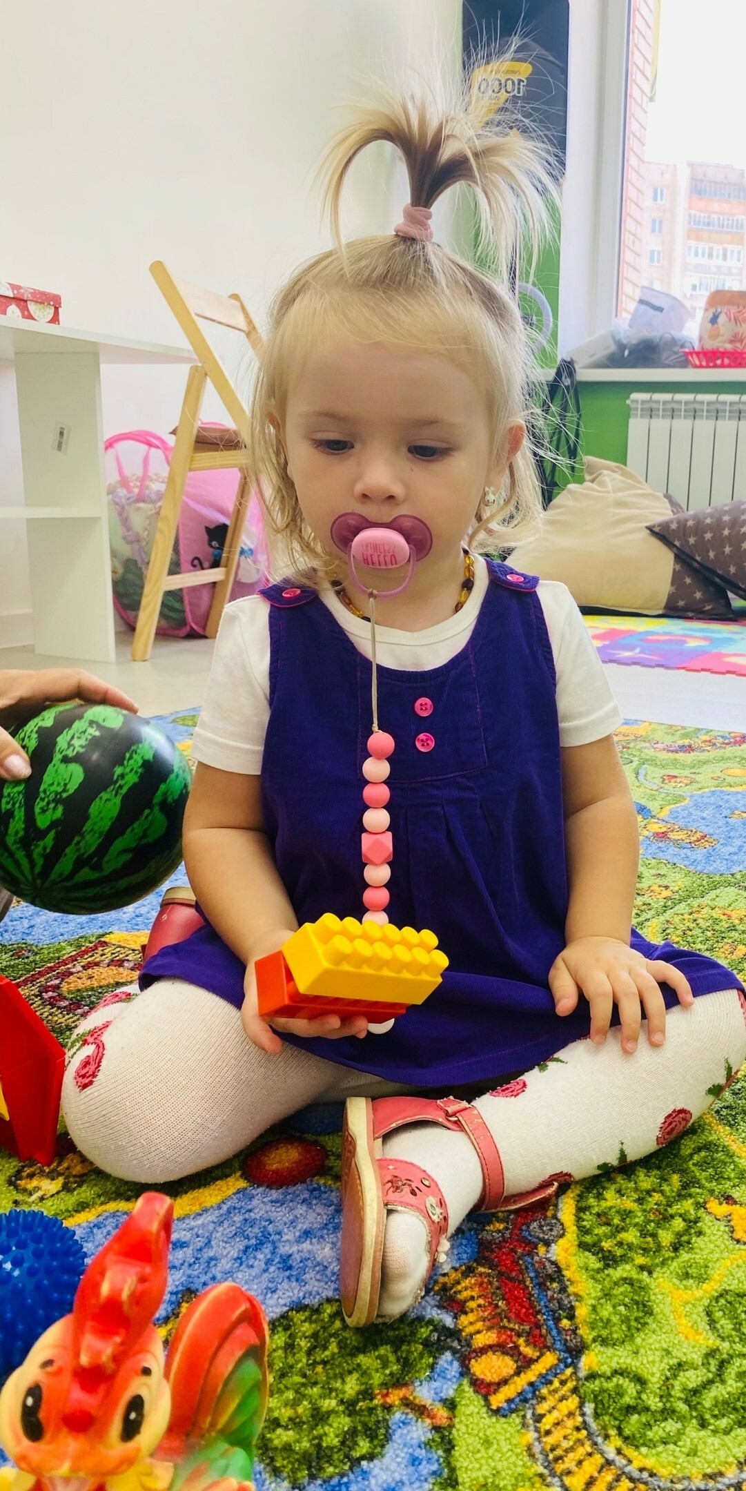 Девочка с соской играет в конструктор в детском ценре