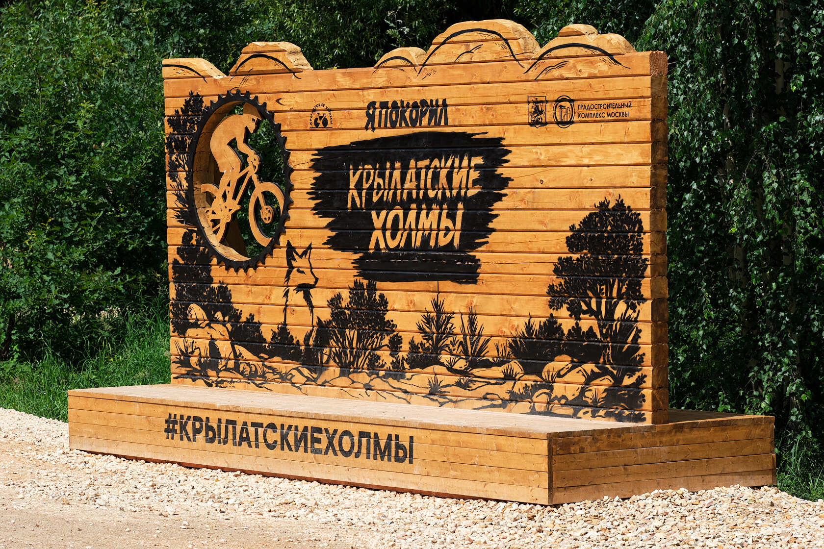 Деревянная фотозона с надписью «Я покорил Крылатские холмы» и силуэтом велосипедиста у трассы