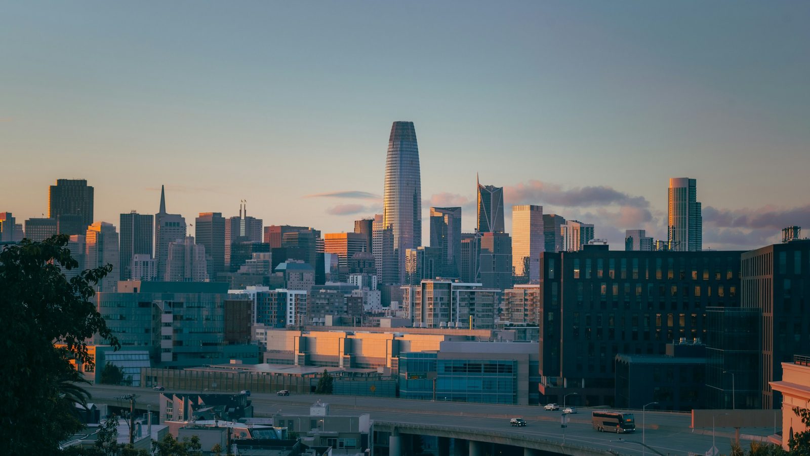 The San Francisco skyline at sunset, with Salesforce Tower and the Transamerica Pyramid above the downtown towers and a freeway in front