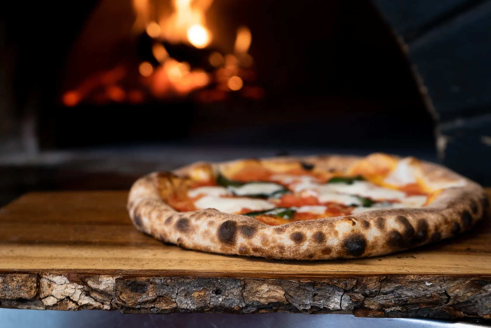 An artisanal wood-fired Neapolitan-style pizza with a perfectly charred crust and fresh mozzarella, shown just outside a blazing brick oven, an authentic preparation common.