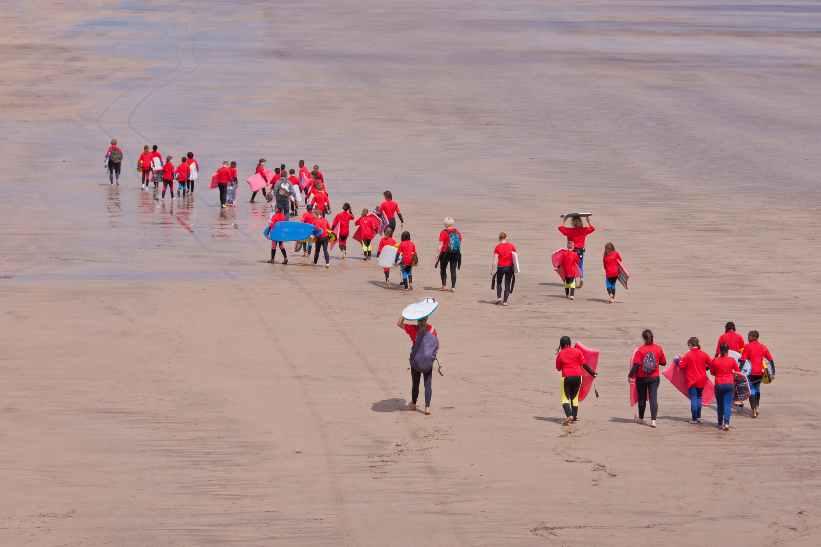 a group of children walking down a beach with surf and body boards